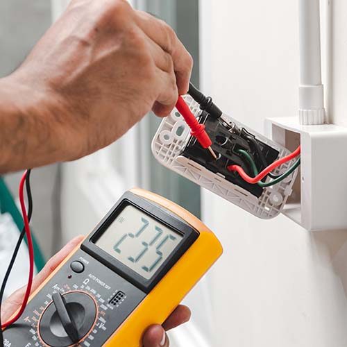 Electrician is using a digital meter to measure the voltage at the power outlet in on the wall.